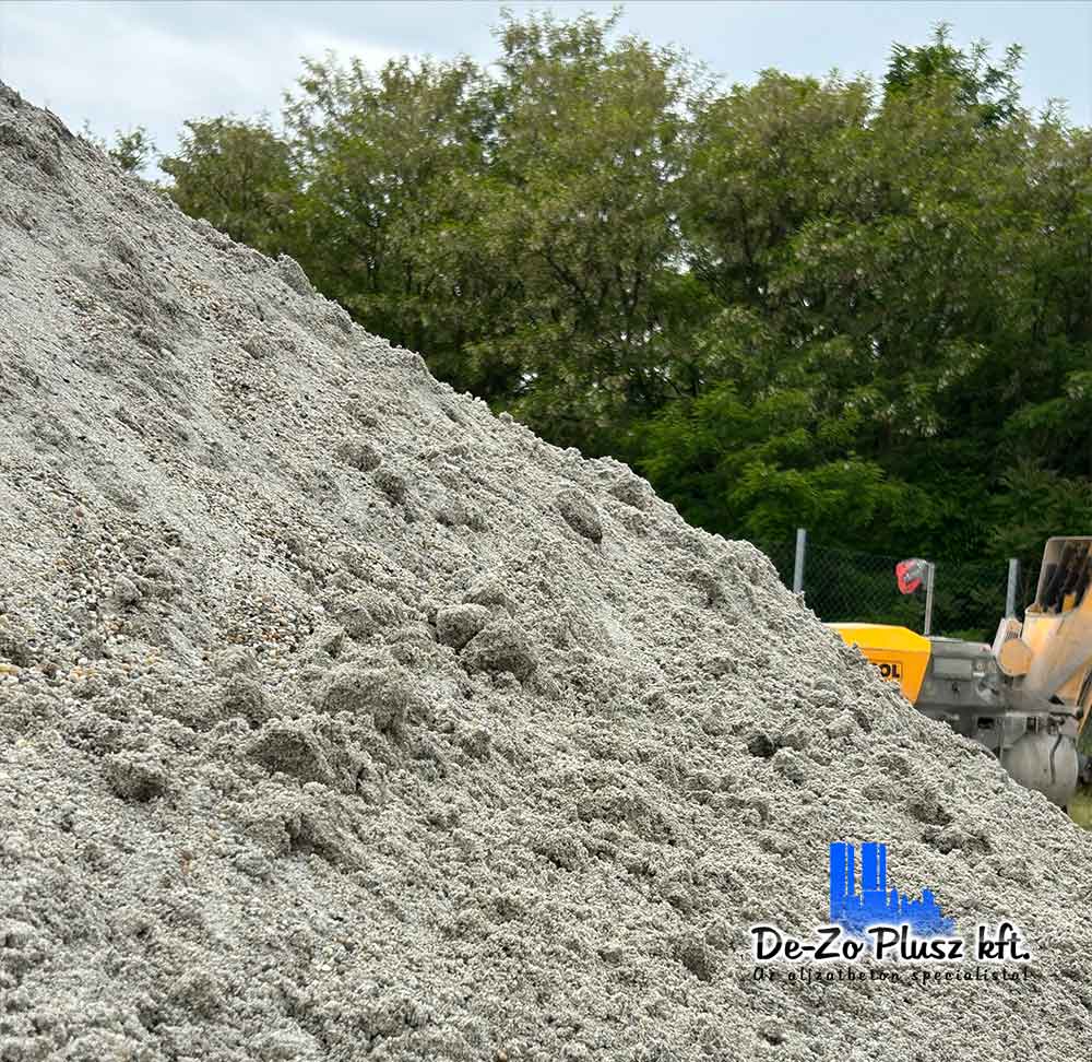 Ez a fotó egy frissen szállított homokos-kavicsos keveréket ábrázol, amely az estrich betonozás egyik kulcsfontosságú alapanyaga. A háttérben munkagépek és zöld környezet is látható, jelezve az élő munkaterületet. A kép hiteles és valós környezetben készült, jól illusztrálva az aljzatbeton előkészítésének egyik legfontosabb lépését.